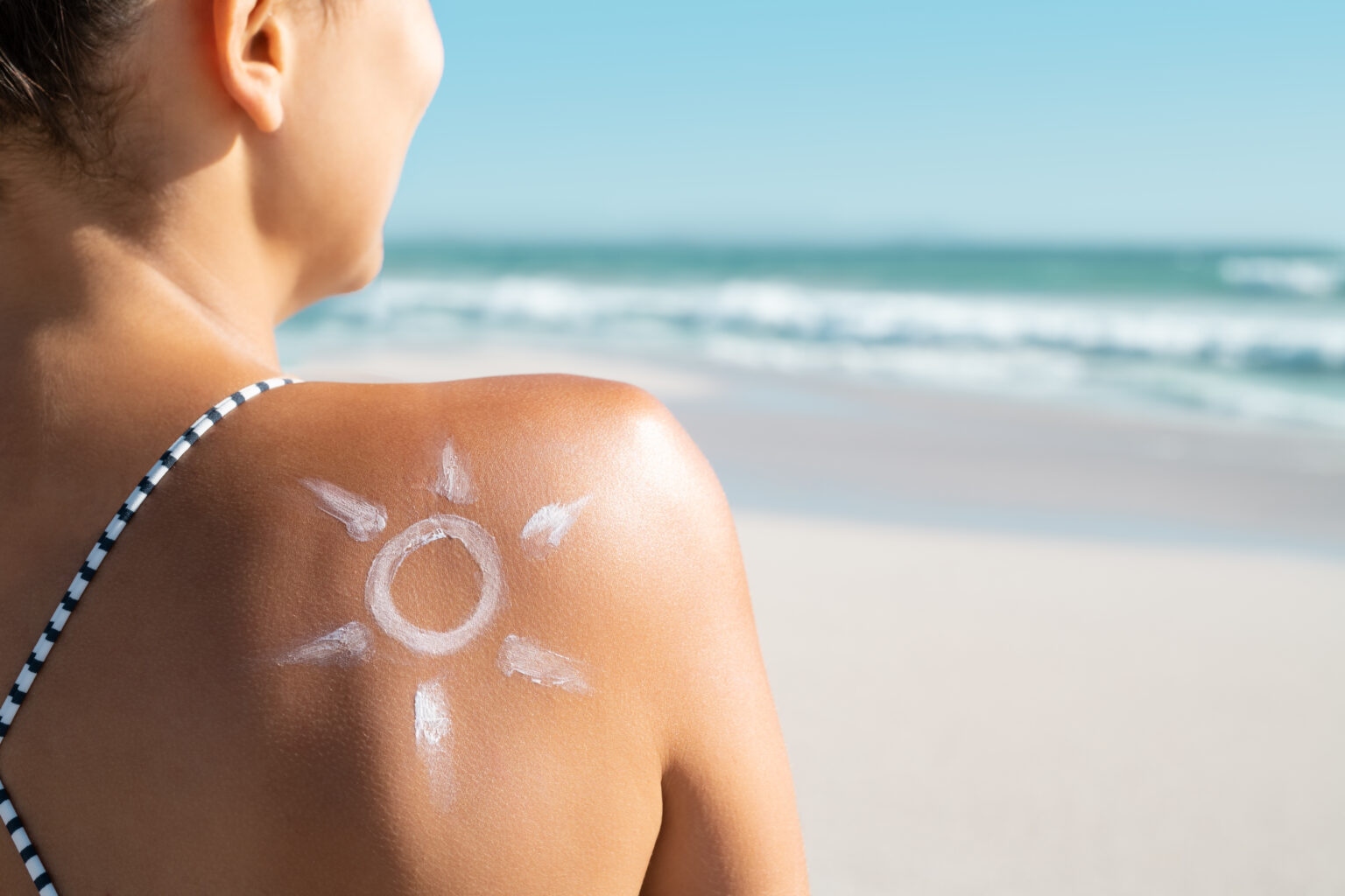 vrouw op het strand met een zon getekend met zonnebrandcrème op de rug